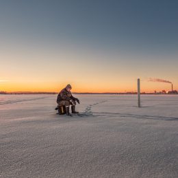 fisherman sitting on stool on ice field