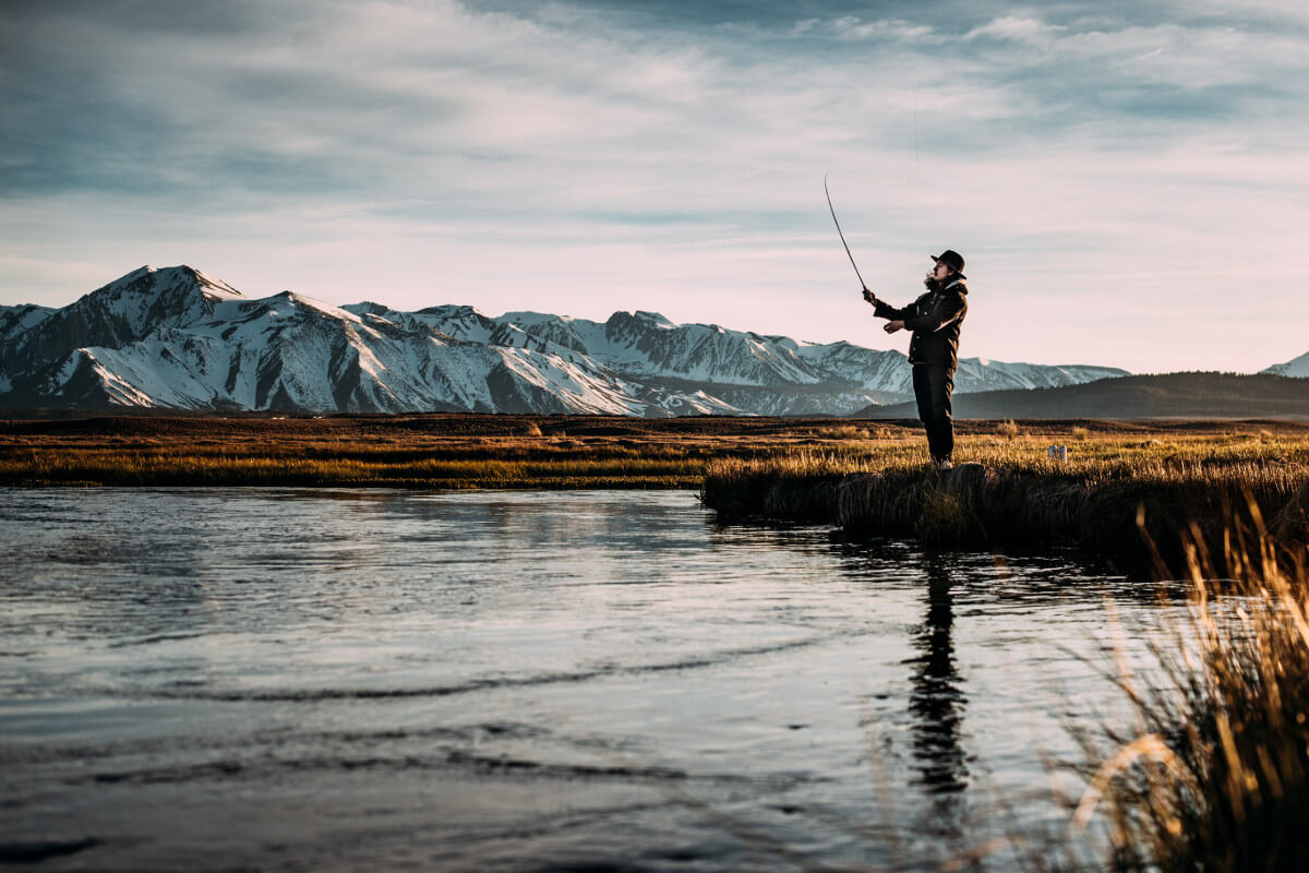 man fishing on river near mountain alps